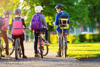 mehrere Kinder mit Rucksack auf dem Fahrrad im Park