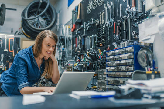 Eine junge Frau steht in einer Werkstatt und schaut auf einen Laptop.