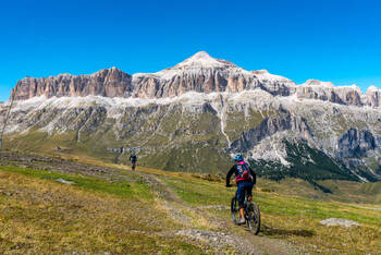 Mountainbiker fahren über eine Wiese in Richtung des Sellastocks der Dolomiten