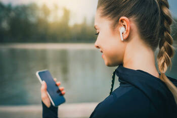 Frau hat AirPods in den Ohren und schaut auf das Smartphone.