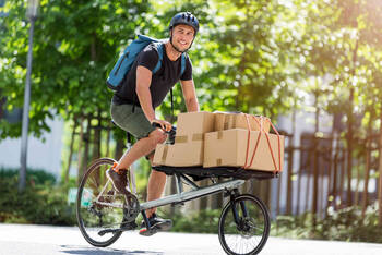 Man fährt auf Cargo-Bike beladen mit Kartons