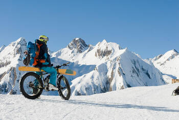 Ein E-Bike Fahrer fährt im Schnee mit seinen Skiern