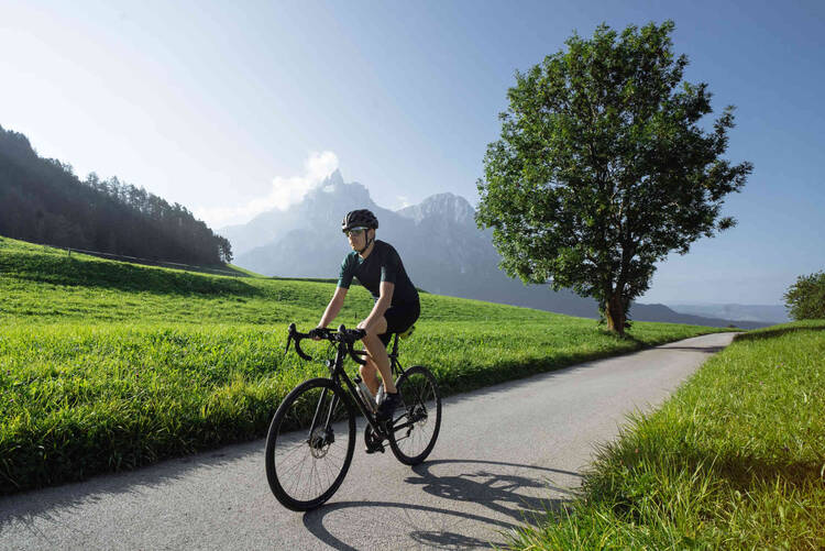 Mann fährt auf Crossbike über eine Straße zwischen einer Wiese her.
