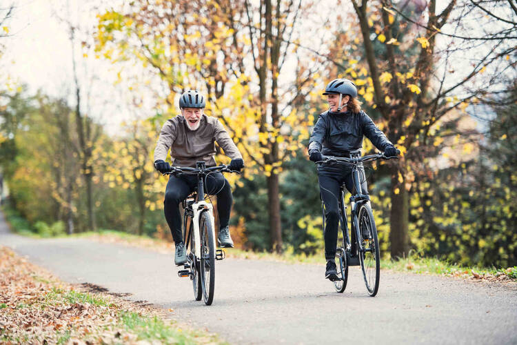 Älterer Mann und ältere Frau fahren Fahrrad und lächeln.