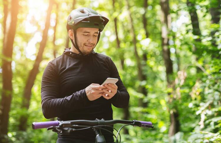 Mann mit Helm auf Fahrrad im Wald hält Handy in der Hand und schaut darauf