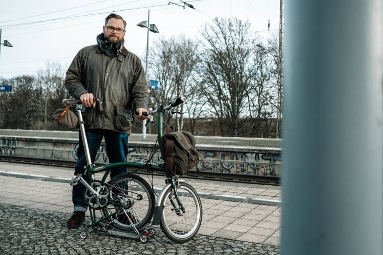 Person steht mit Faltrad vom Brompton am Bahnsteig