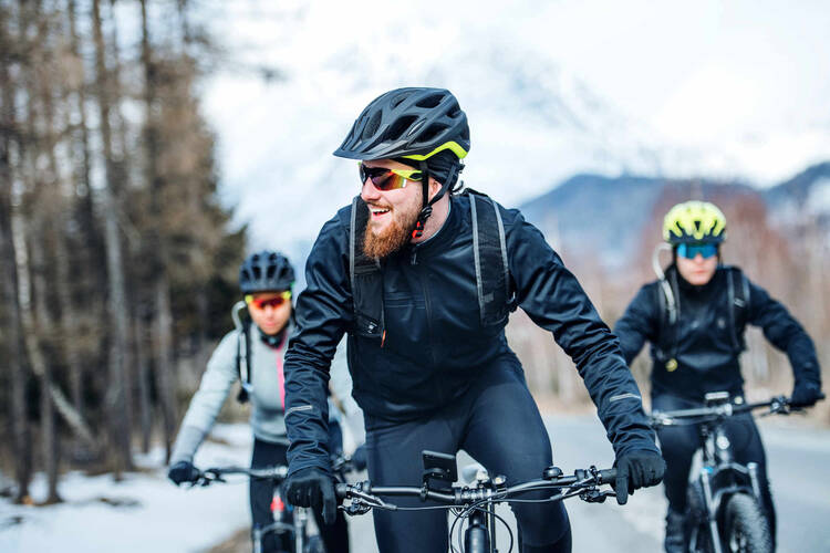 drei Fahrradfahrer mit Helm fahren im Winter auf Straße.