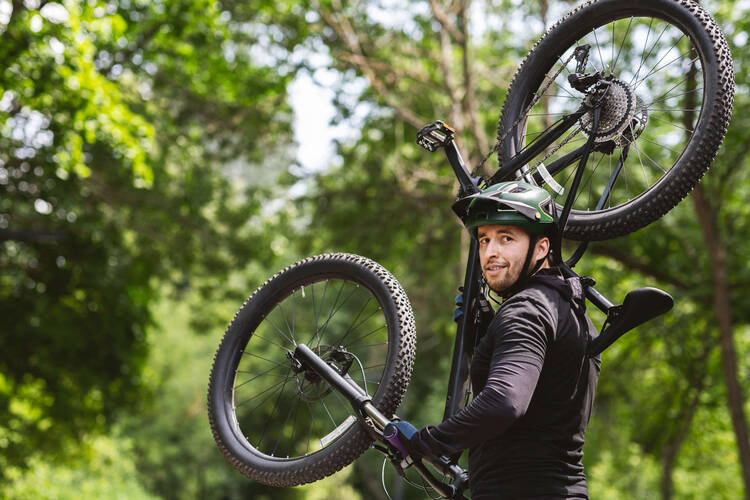 Mann trägt Mountainbike auf Schulter