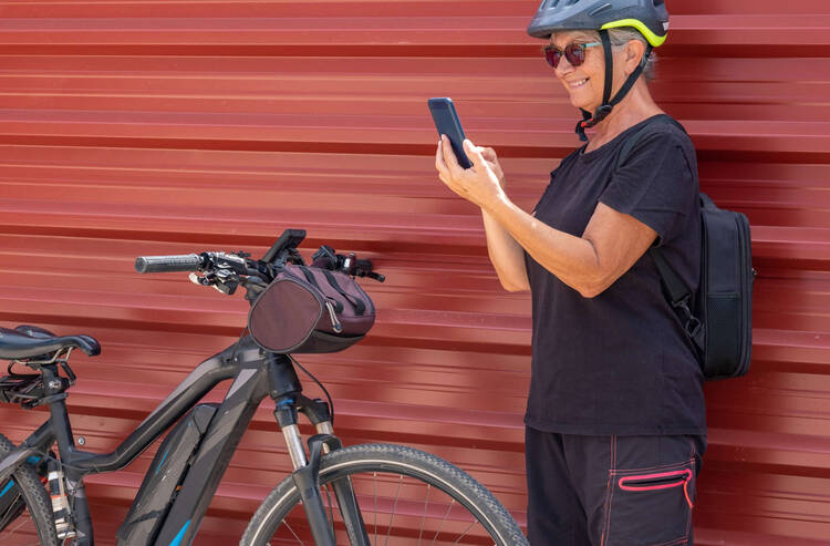 Eine Frau steht vor ihrem E-Bike und schaut auf ihr Handy