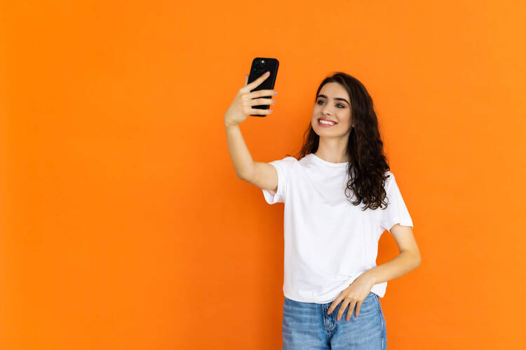WhatsApp Avatare – Funktion & wie sie erstellt werden Frau macht Selfie vor orangem Hintergrund
