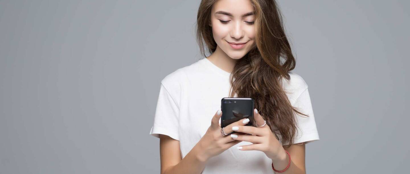 Ein Mädchen schaut lächelnd auf ihr Smartphone