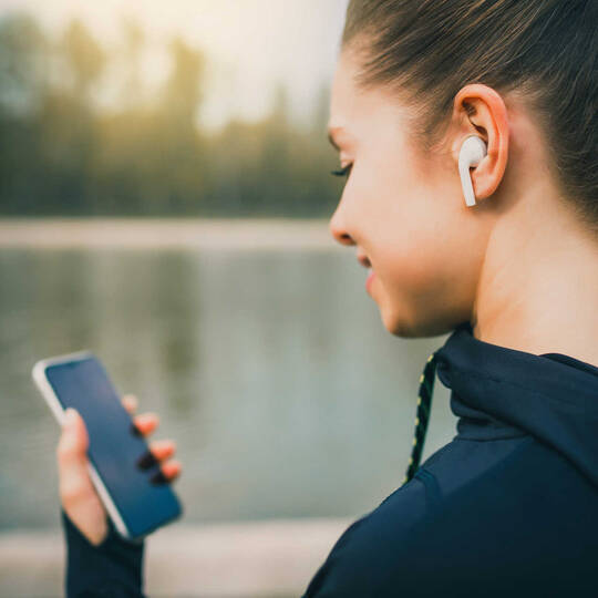 Frau hat AirPods in den Ohren und schaut auf das Smartphone.