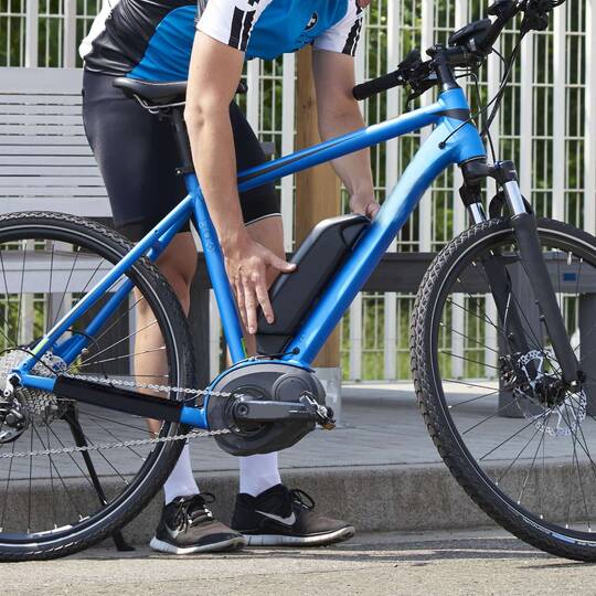 Mann hält die Hände an den Akku eines blauen E-Bikes