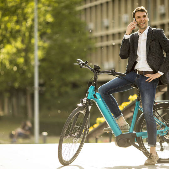 Mann sitzt auf einem stehenden E-Bike und telefoniert