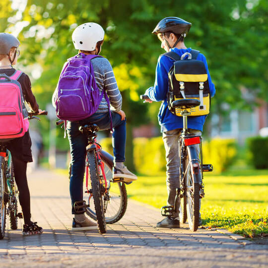mehrere Kinder mit Rucksack auf dem Fahrrad im Park