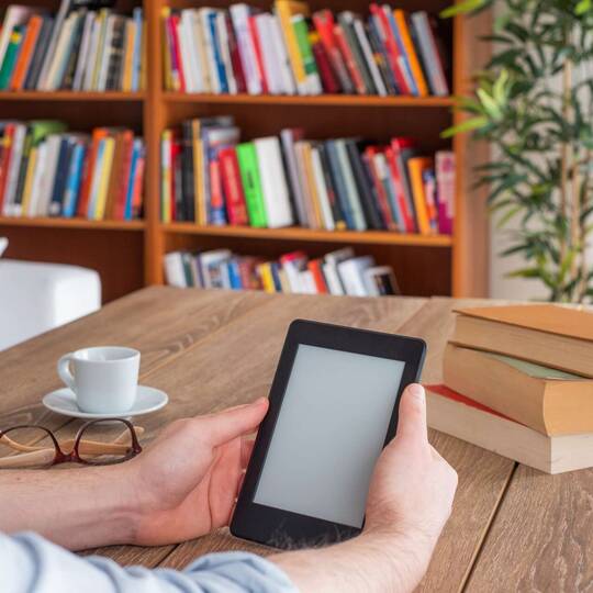 Kindle in gemütlicher Umgebung von zwei Händen gehalten