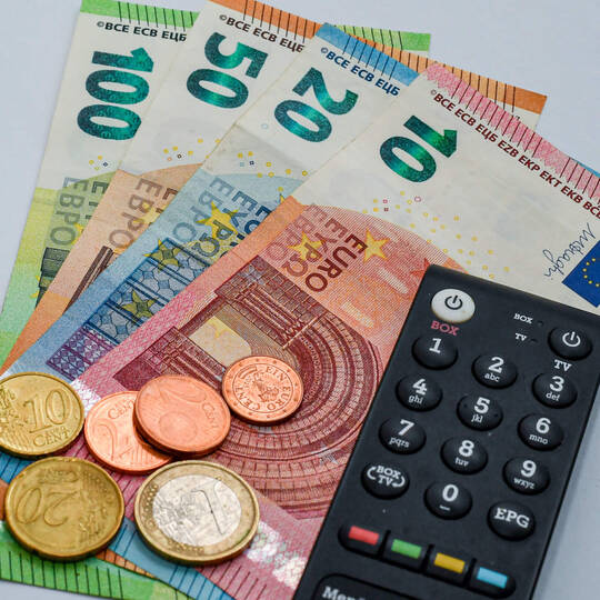 Der ORF-Beitrag: die Haushaltsabgabe ab 2024 Geld mit Fernbedienung auf dem Tisch