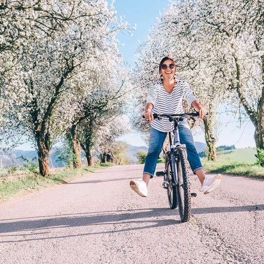 Frau fährt lachend auf dem Fahrrad im Frühling