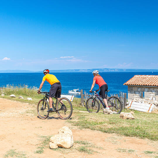 Zwei Personen fahren am Strand Fahrrad