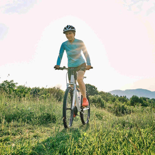 Frau fährt mit Mountainbike über Wiese.